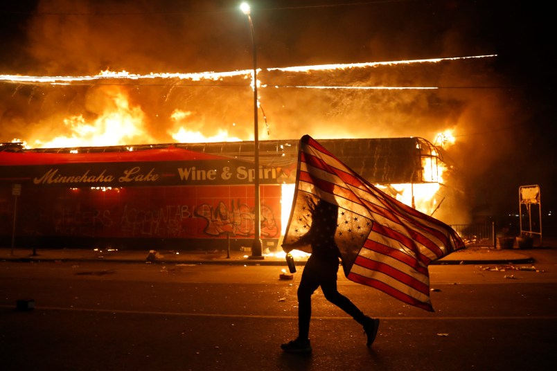 A protester carries the carries the U.S. flag upside, a sign of distress, Thursday, May 28, 2020, in Minneapolis. Violent protests over the death of George Floyd, the black man who died in police custody broke out in Minneapolis for a third straight night. (AP Photo/Julio Cortez)
