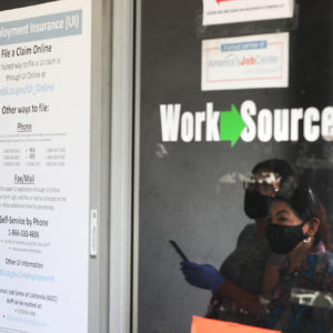 CANOGA PARK, CA - MAY 14: Estella Flores, right, and Maria Mora, left, are reflected in a window as they look for information in front of the closed California State Employment Development Department on Thursday, May 14, 2020 in Canoga Park, CA. (Brian van der Brug / Los Angeles Times)