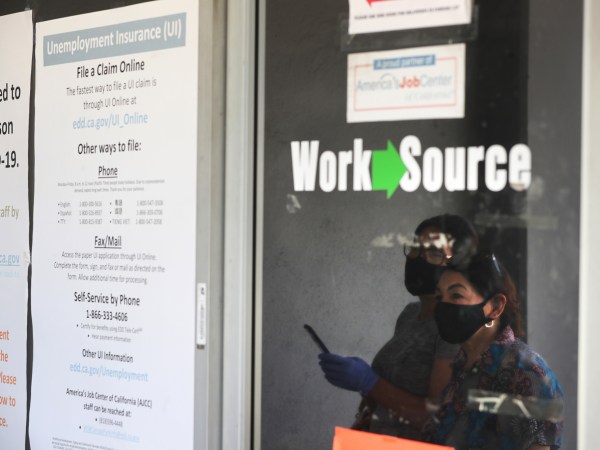 CANOGA PARK, CA - MAY 14: Estella Flores, right, and Maria Mora, left, are reflected in a window as they look for information in front of the closed California State Employment Development Department on Thursday, May 14, 2020 in Canoga Park, CA. (Brian van der Brug / Los Angeles Times)