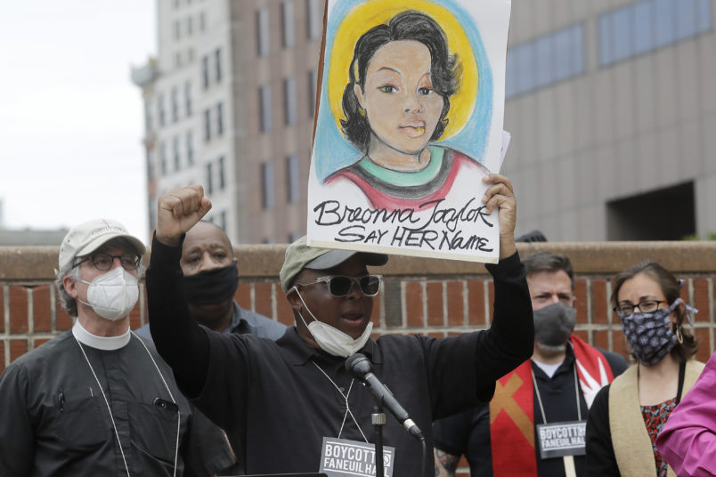 Kevin Peterson, founder and executive director of The New Democracy Coalition, center, displays a placard showing fallen Breonna Taylor as he addresses a rally, Tuesday, June 9, 2020, in Boston. Petersen advocates for changing the name of Faneuil Hall, as its namesake Peter Faneuil, was a slave owner. (AP Photo/Steven Senne)