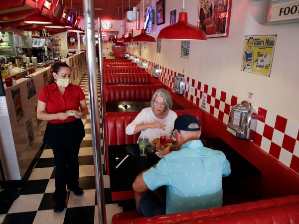 FILE - In this May 21, 2020, file photo, Lynn Tanner, center, and her husband Ryan, bottom right, are served lunch at Busy Bee Cafe in Ventura, Calif. Heading into Memorial Day weekend, California's mood was celebratory. The state had avoided dire predictions of a coronavirus surge, hospitalizations were declining, restaurants and most other businesses had reopened. As July 4th approaches, the mood has soured. Infection rates and hospitalizations are rising fast. Most bars have been ordered closed along with inside dining at restaurants. Many beaches are off-limits or have restrictions to limit crowds. Fireworks shows are canceled and Gov. Gavin Newsom is imploring Californians to avoid the holiday tradition of backyard barbecues and other gatherings of relatives and friends. (AP Photo/Marcio Jose Sanchez, File)