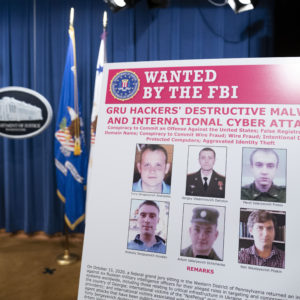 A poster showing six wanted Russian military intelligent officers is displayed before a news conference at the Department of Justice, Monday, Oct. 19, 2020, in Washington. (AP Photo/Andrew Harnik, pool)