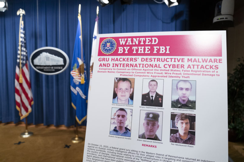 A poster showing six wanted Russian military intelligent officers is displayed before a news conference at the Department of Justice, Monday, Oct. 19, 2020, in Washington. (AP Photo/Andrew Harnik, pool)