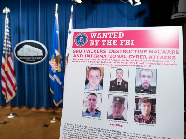 A poster showing six wanted Russian military intelligent officers is displayed before a news conference at the Department of Justice, Monday, Oct. 19, 2020, in Washington. (AP Photo/Andrew Harnik, pool)