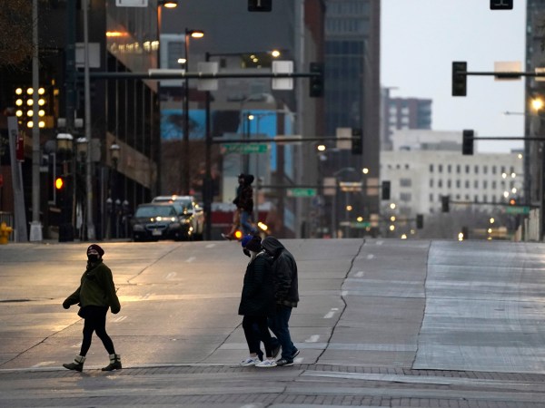 Pedestrians wear masks while crossing an empty road at the intersection of Market Street and 15th Avenue during the evening rush hour Monday, Dec. 28, 2020, in downtown Denver. (AP Photo/David Zalubowski)