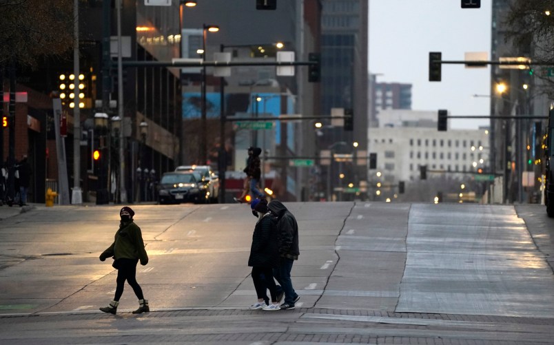 Pedestrians wear masks while crossing an empty road at the intersection of Market Street and 15th Avenue during the evening rush hour Monday, Dec. 28, 2020, in downtown Denver. (AP Photo/David Zalubowski)