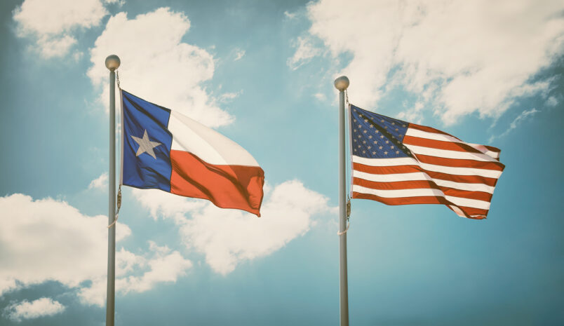 The state flag of Texas and American flag waving in the wind on flagpoles