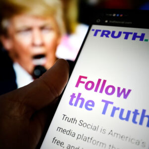 The TRUTH Social website is seen on a mobile device with an image of former US president Donald Trump in the background in this photo illustration in Warsaw, Poland on 23 February, 2022. TRUTH Social is a newly developed social media platform by the Trump Media and Technology Group (TMTG) modelled after Twitter. The initiative was taken after Trump himself had been banned from Facebook and Twitter in 2021. (Photo by STR/NurPhoto)