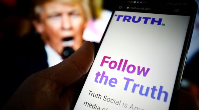 The TRUTH Social website is seen on a mobile device with an image of former US president Donald Trump in the background in this photo illustration in Warsaw, Poland on 23 February, 2022. TRUTH Social is a newly developed social media platform by the Trump Media and Technology Group (TMTG) modelled after Twitter. The initiative was taken after Trump himself had been banned from Facebook and Twitter in 2021. (Photo by STR/NurPhoto)