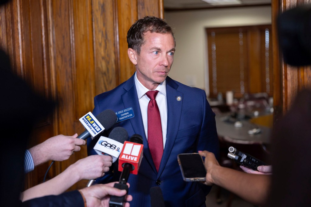 Greg Dolezal stands among reporters in a hallway at the Georgia State Capitol, speaking into microphones.